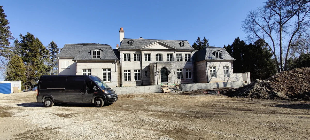 A stone home under construction, with a work van and unfinished site in front