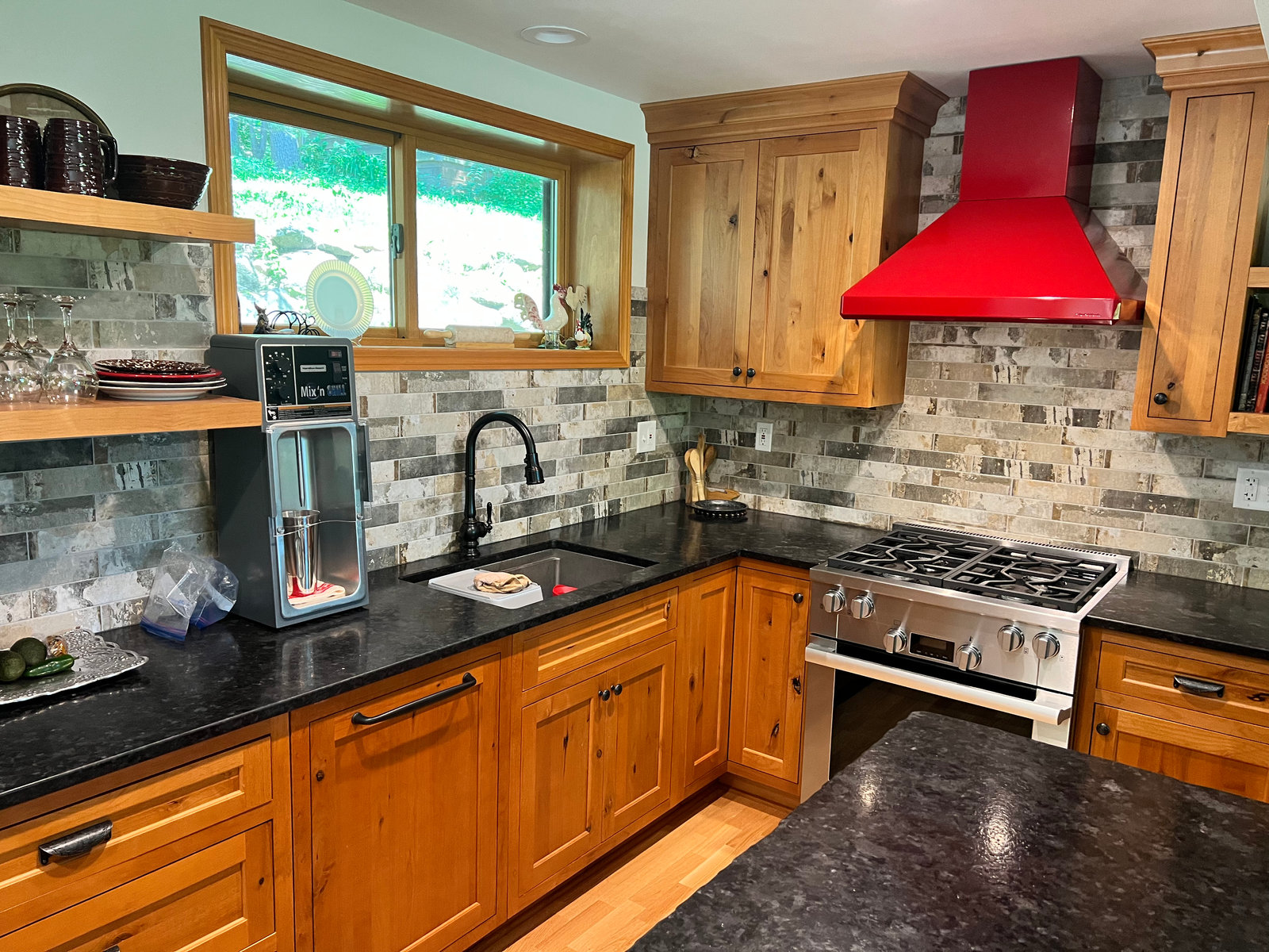 Warm wood cabinetry, dark countertops, and a red range hood