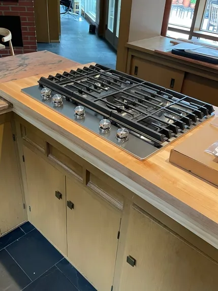A stainless steel gas cooktop fitted into a wood countertop.