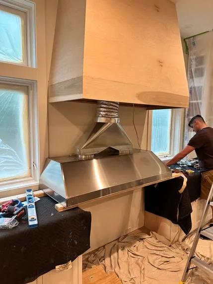 A stainless steel hood liner being installed within a custom wood hood