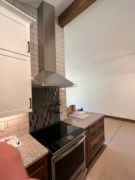 A stainless steel range and chimney hood surrounded by white cabinetry.