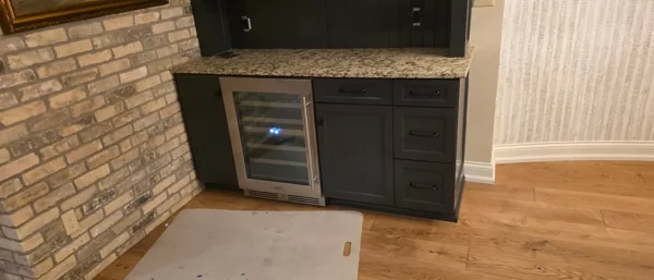 An undercounter refrigerator fitted into a bar with dark cabinetry.
