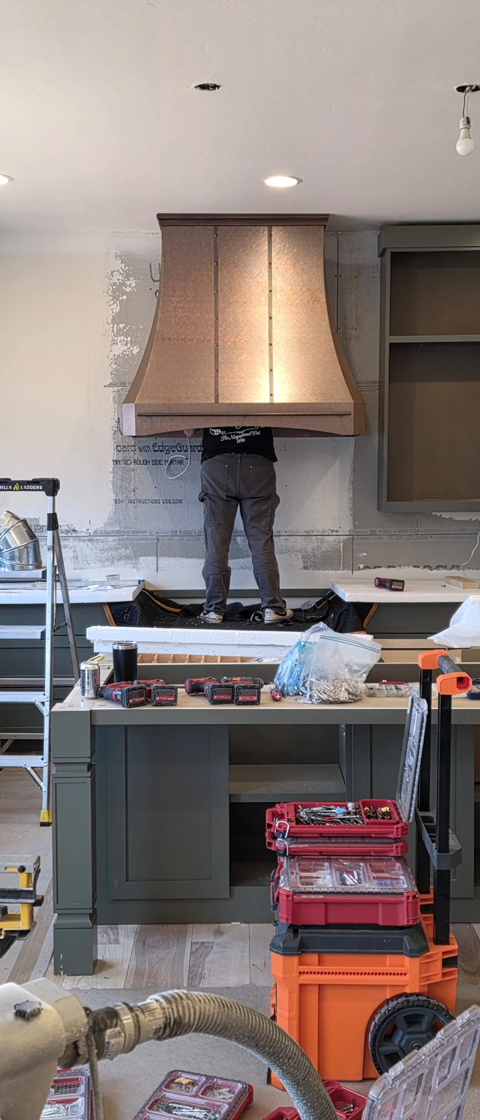 An installer working beneath a copper range hood during a kitchen renovation